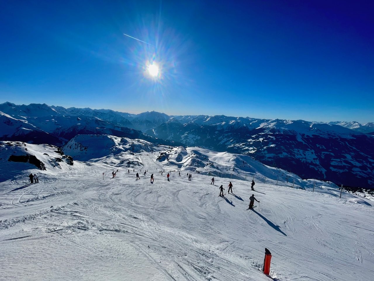 Skifahrer auf einer sonnigen Piste vor einem Alpenpanorama